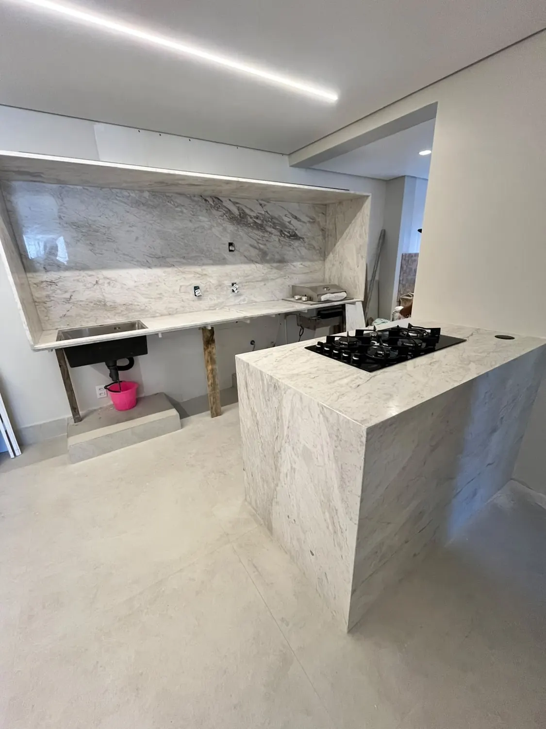Cozinha com ilha e cooktop revestida em pedra, trabalho da WK Mármores